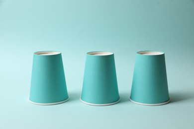Photo of Three paper cups on light blue background. Thimblerig game