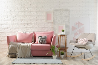 Stylish living room interior with sofa and rocking armchair near brick wall