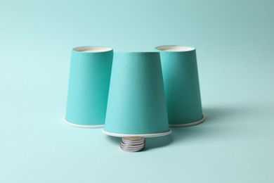 Three paper cups and coins on light blue background. Thimblerig game
