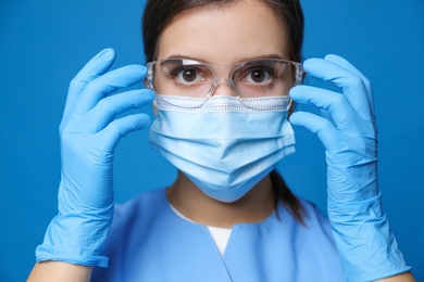 Photo of Doctor in protective mask, medical gloves and glasses against blue background