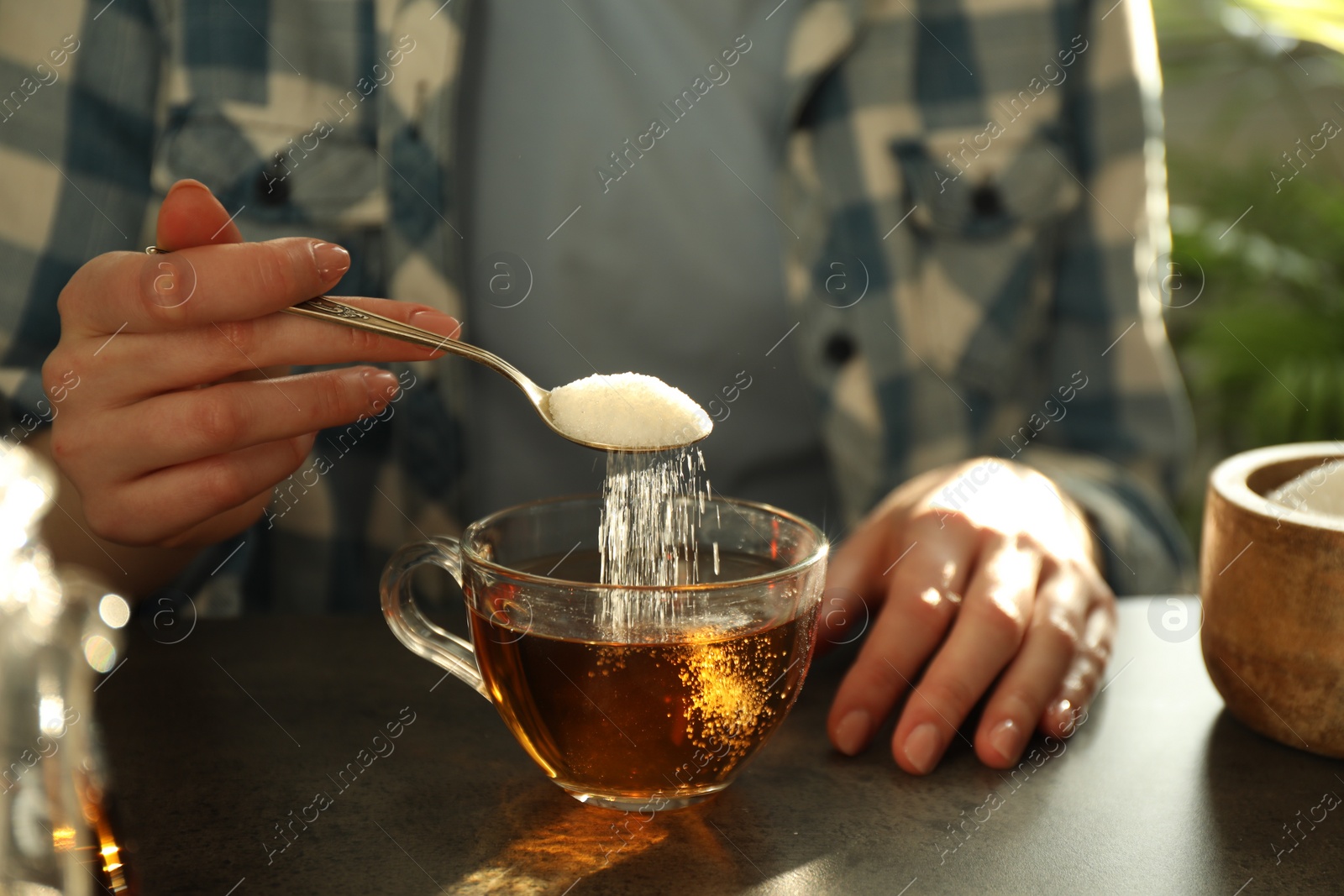 Photo of Woman adding sugar into cup of tea at dark table, closeup