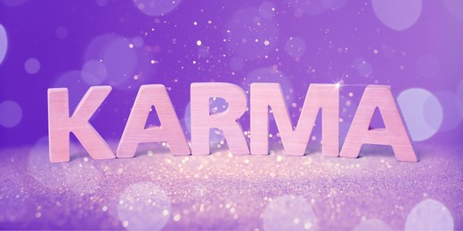 Word Karma made of wooden letters on shiny glitter against violet background. Banner design