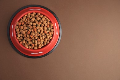 Photo of Dry dog food in feeding bowl on brown background, top view. Space for text