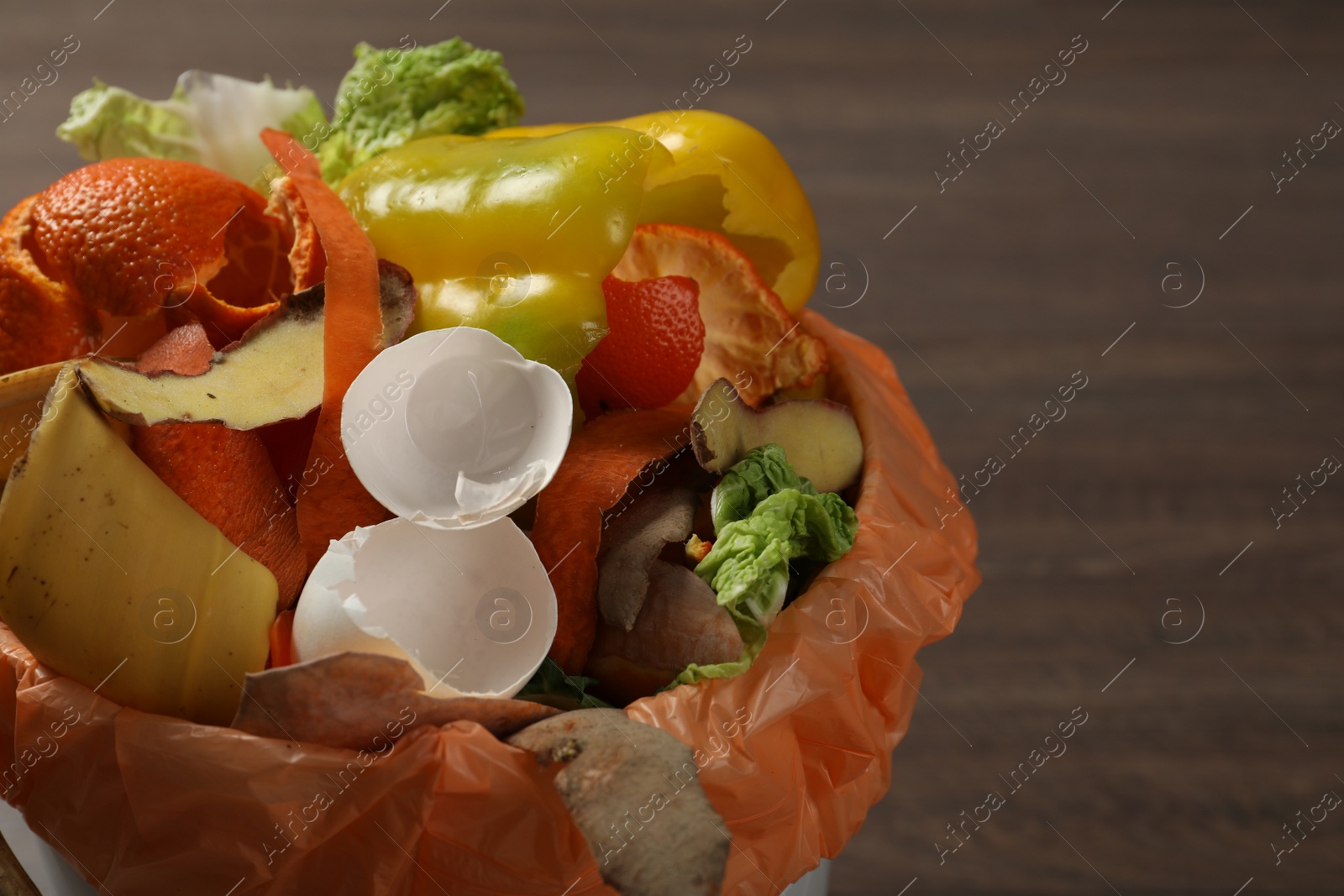 Photo of Trash bin with organic waste for composting on wooden background, closeup