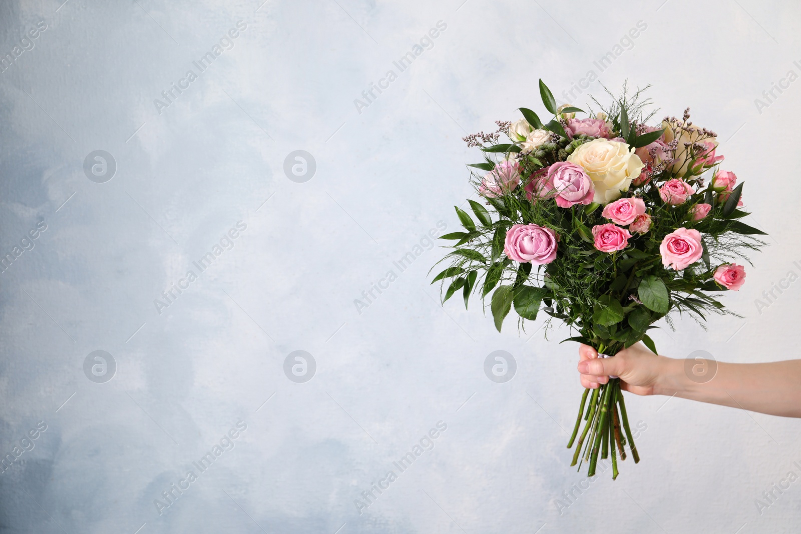 Photo of Woman with bouquet of beautiful roses on light blue background, closeup. Space for text