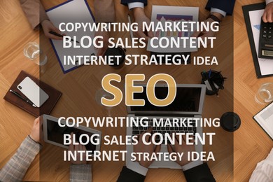 Image of Search engine optimization (SEO). Many terms above marketing team developing strategy of internet promotion at wooden table, top view
