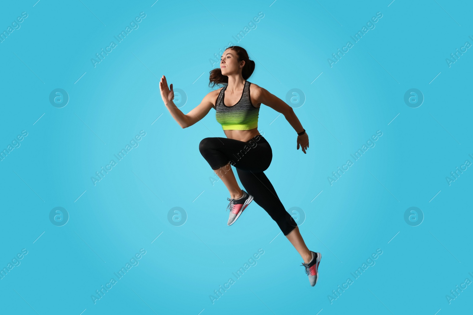 Photo of Athletic young woman running on light blue background, side view