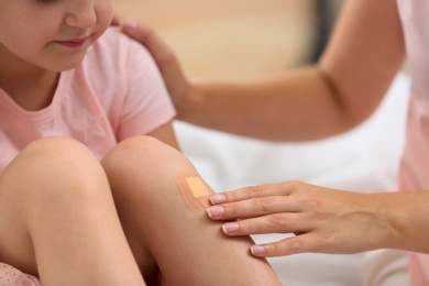 Photo of Woman applying plaster on girl's knee, closeup view