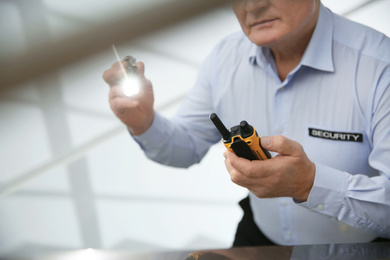 Photo of Professional security guard with flashlight and portable radio set indoors, closeup