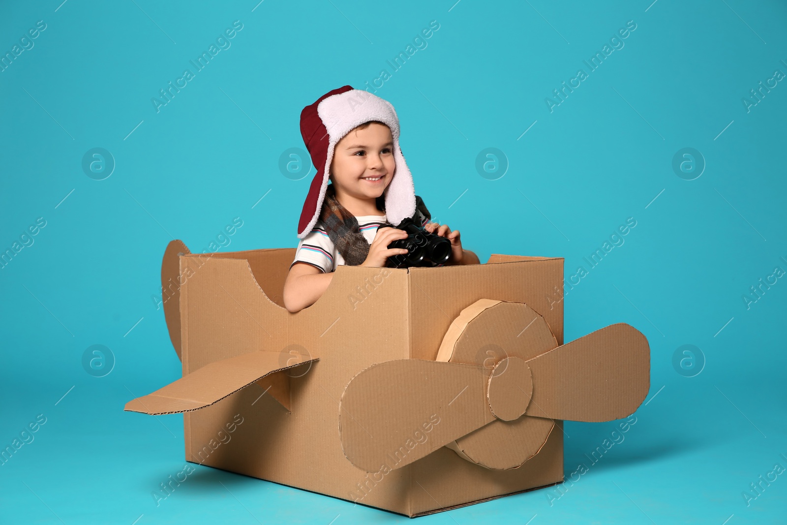 Photo of Cute little boy playing with binoculars and cardboard airplane on color background