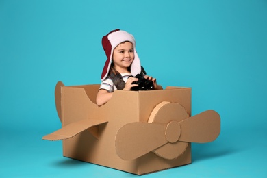 Cute little boy playing with binoculars and cardboard airplane on color background