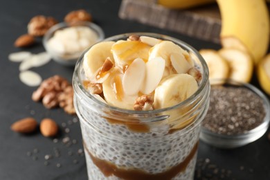 Photo of Delicious chia pudding with banana, walnuts and caramel sauce in glass on table, closeup