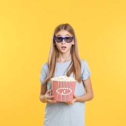Emotional teenage girl with 3D glasses and popcorn during cinema show on color background