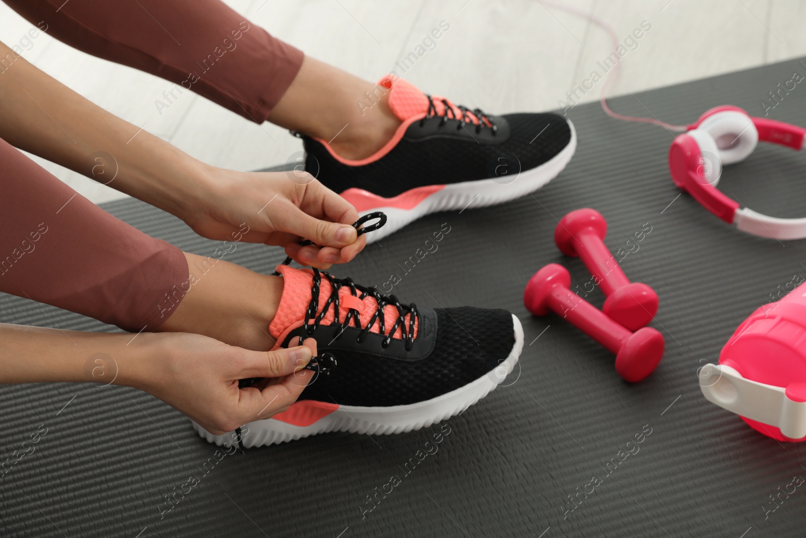 Photo of Woman tying sneaker's shoelaces on exercise mat, closeup
