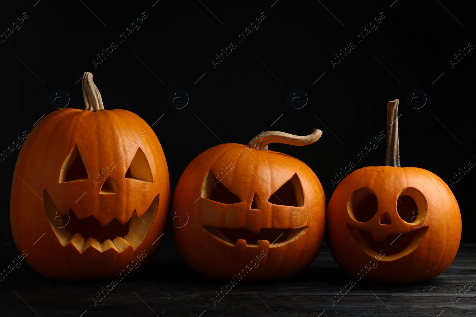 Photo of Scary jack o'lanterns made of pumpkins on wooden table against black background. Halloween traditional decor