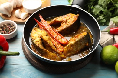 Photo of Tasty fish curry in frying pan and ingredients on light blue wooden table, closeup. Indian cuisine