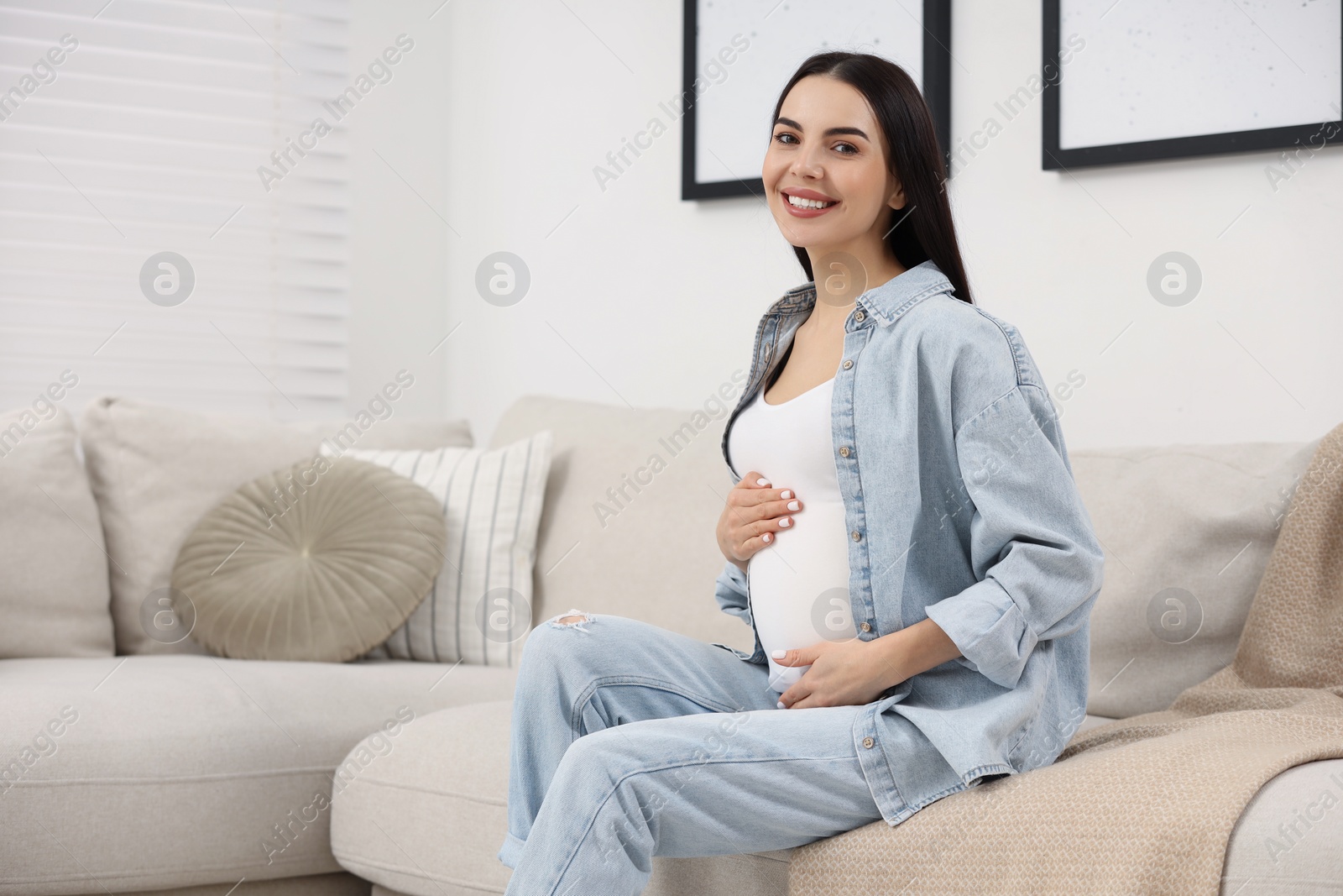 Photo of Happy pregnant woman on sofa at home, space for text