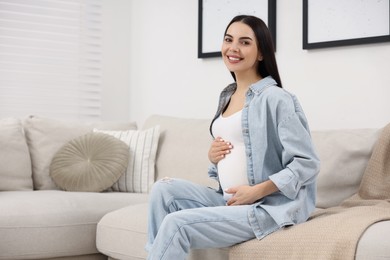 Happy pregnant woman on sofa at home, space for text