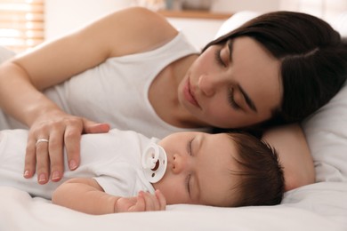 Photo of Young mother resting near her sleeping baby on bed at home, closeup