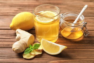 Photo of Glass with hot tea, lemon and ginger as cold remedies on wooden table