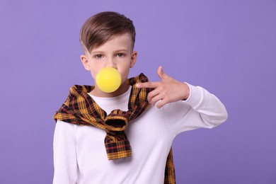 Boy blowing bubble gum on purple background