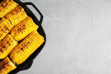 Photo of Fresh grilled tasty corn cobs in pan and space for text on light background, top view