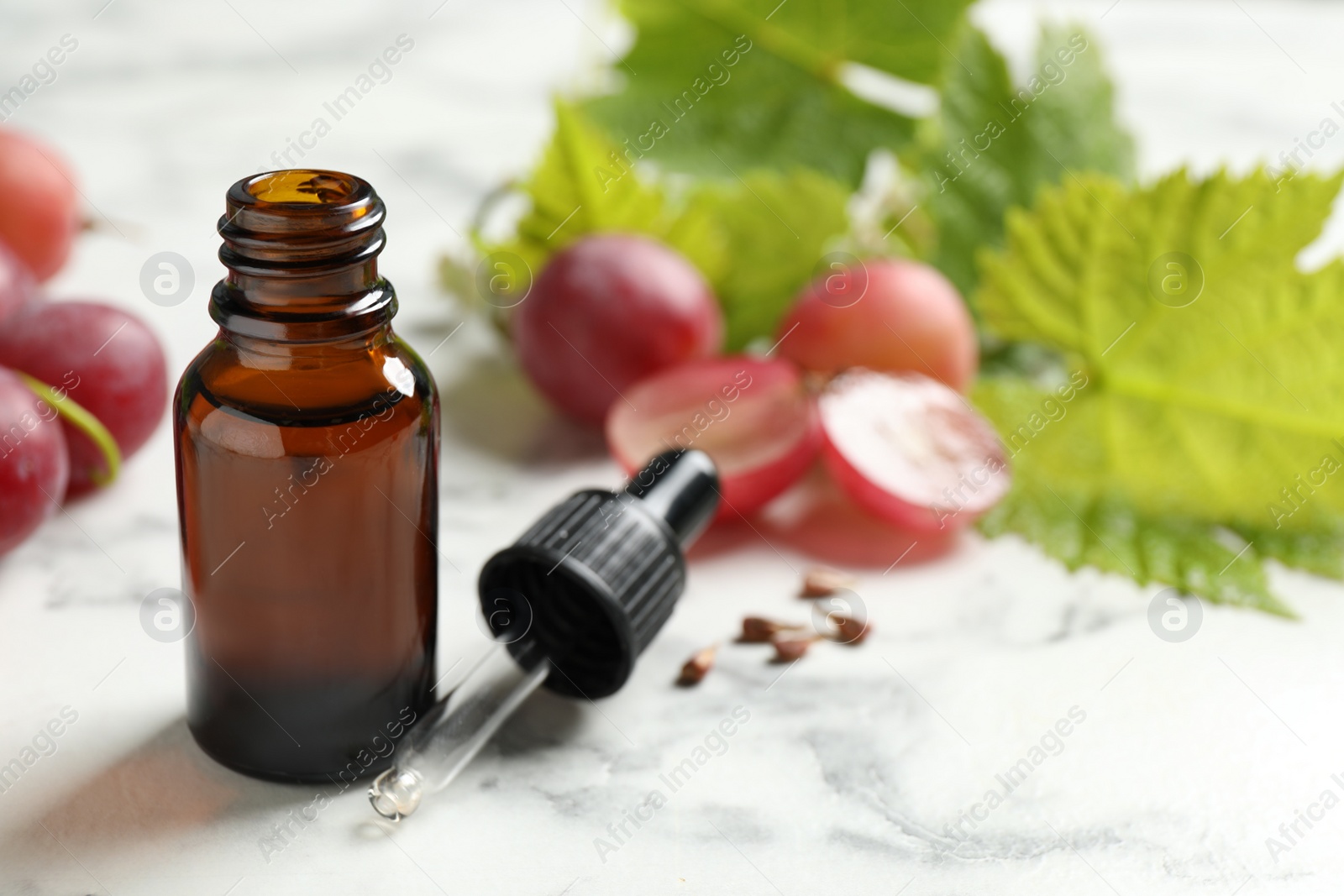 Photo of Bottle of natural grape seed oil on white marble table. Organic cosmetic