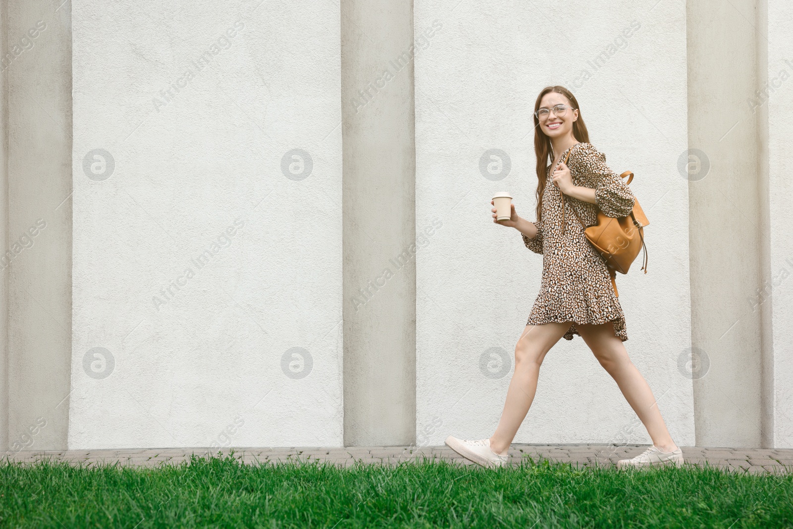 Photo of Young woman with cup of drink walking near stone wall outdoors, space for text