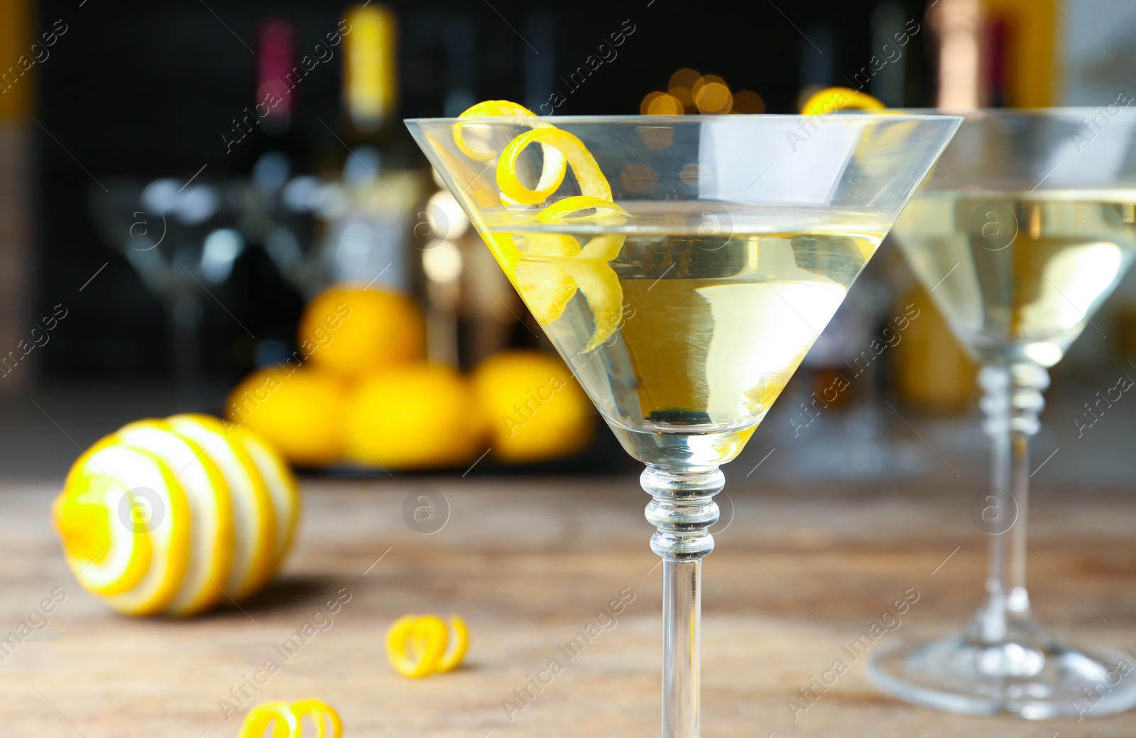 Photo of Glass of Lemon Drop Martini cocktail with zest on table against blurred background, closeup. Space for text