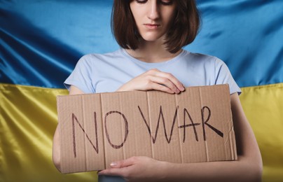 Photo of Sad woman holding poster with words No War near Ukrainian flag