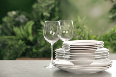 Set of clean dishware and wineglasses on grey table against blurred background