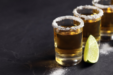 Mexican Tequila shots, lime slices and salt on grey table. Space for text