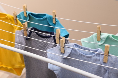 Photo of Different cute baby onesies hanging on clothes line against beige background. Laundry day