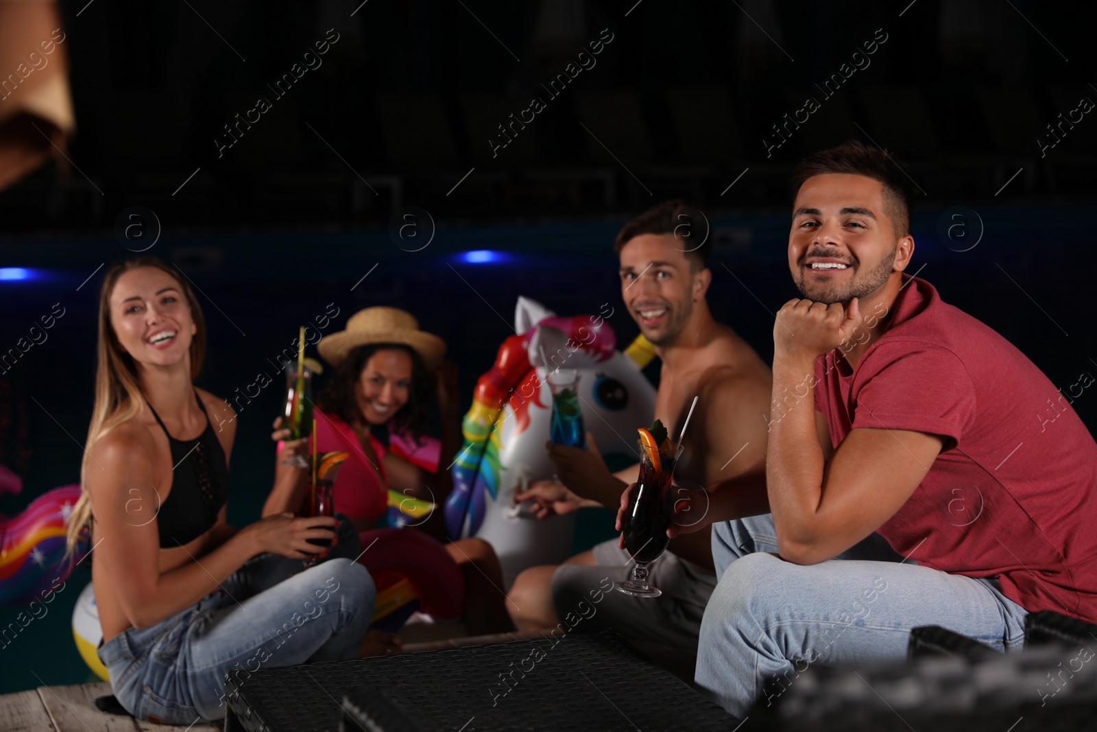 Photo of Happy young friends with refreshing cocktails relaxing near outdoor pool at night