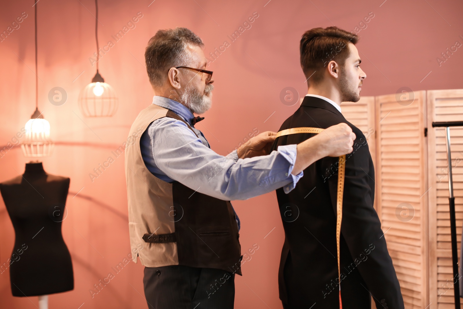 Photo of Mature tailor taking client's measurements in atelier