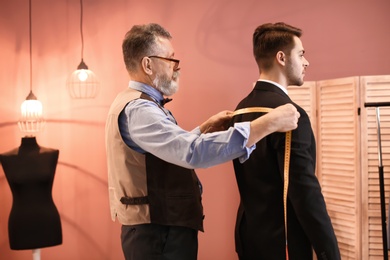 Photo of Mature tailor taking client's measurements in atelier