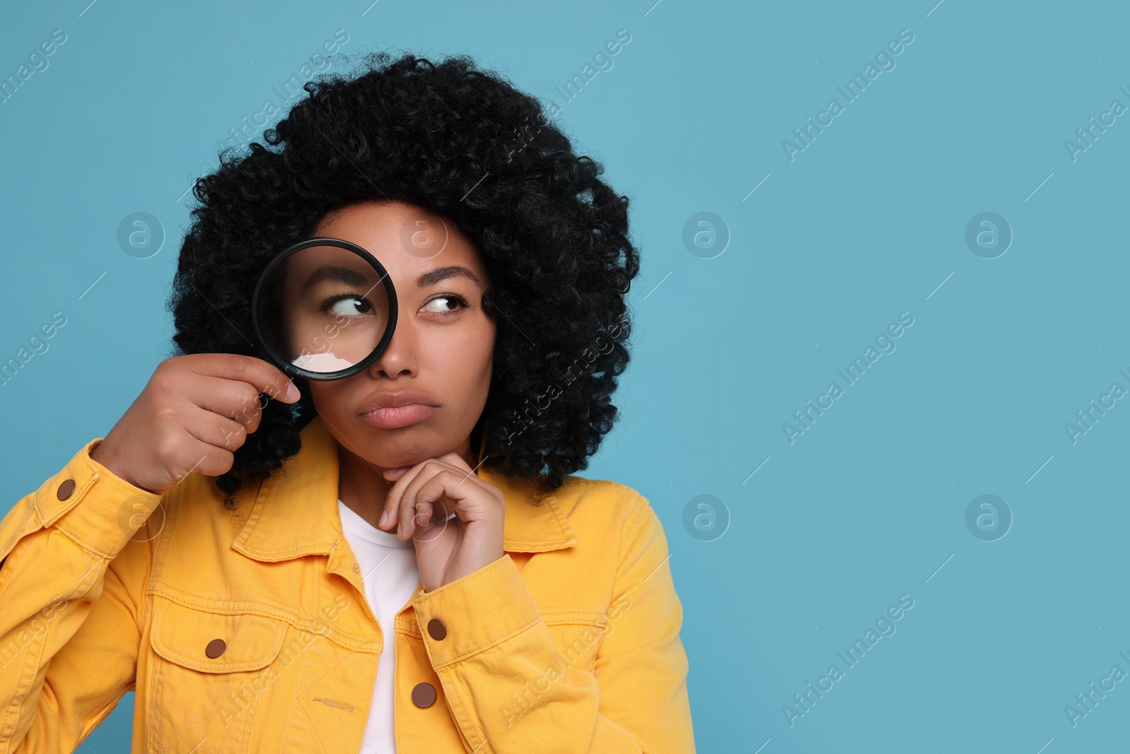 Photo of Woman looking through magnifier glass on light blue background, space for text