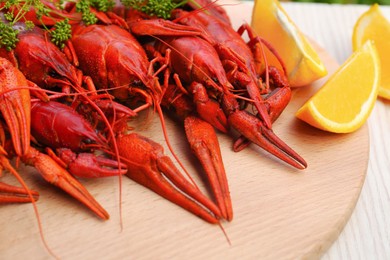 Photo of Delicious red boiled crayfish and orange on wooden board, closeup