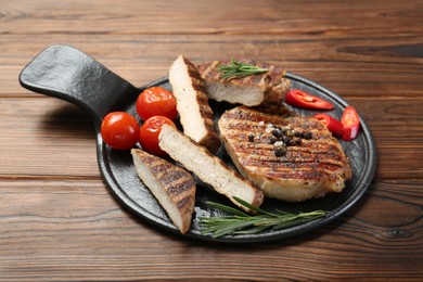 Photo of Grilled pork steaks with rosemary, spices and vegetables on wooden table