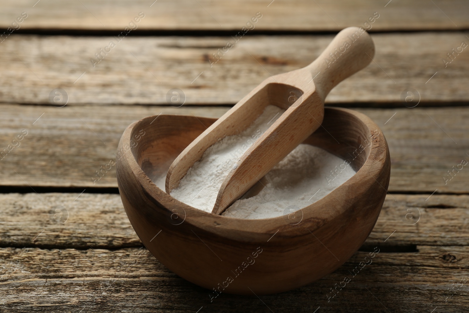 Photo of Baking powder in bowl and scoop on wooden table, closeup