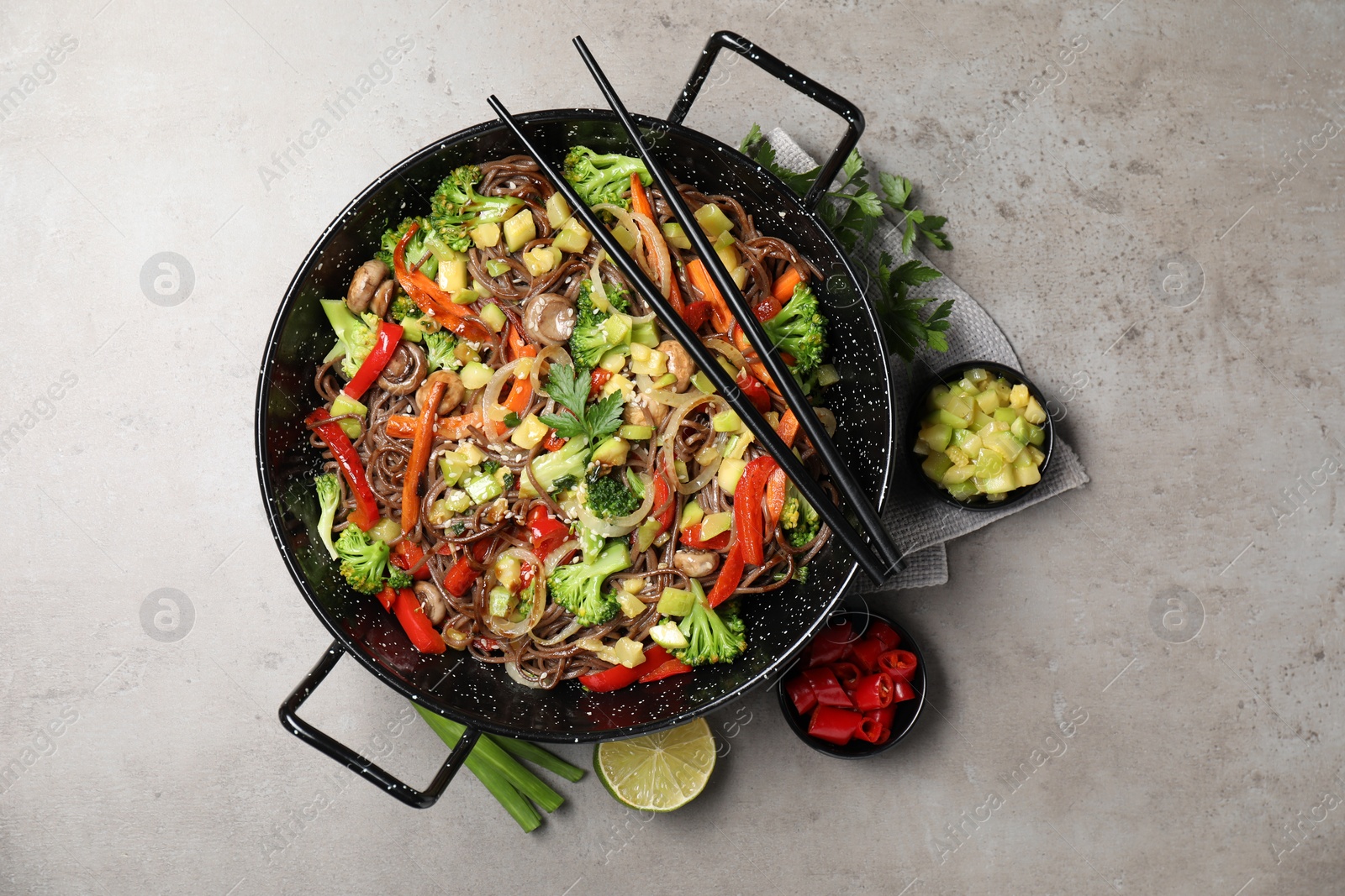 Photo of Stir-fry. Tasty noodles with meat in wok, chopsticks and ingredients on grey textured table, flat lay