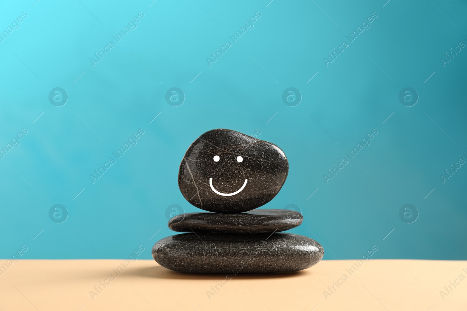 Photo of Stack of stones with drawn happy face on beige table against light blue background. Zen concept