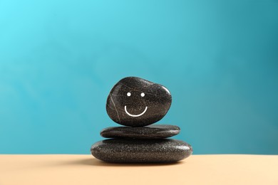 Photo of Stack of stones with drawn happy face on beige table against light blue background. Zen concept