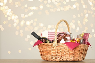 Photo of Wicker basket with gifts, wine and food against blurred festive lights. Space for text