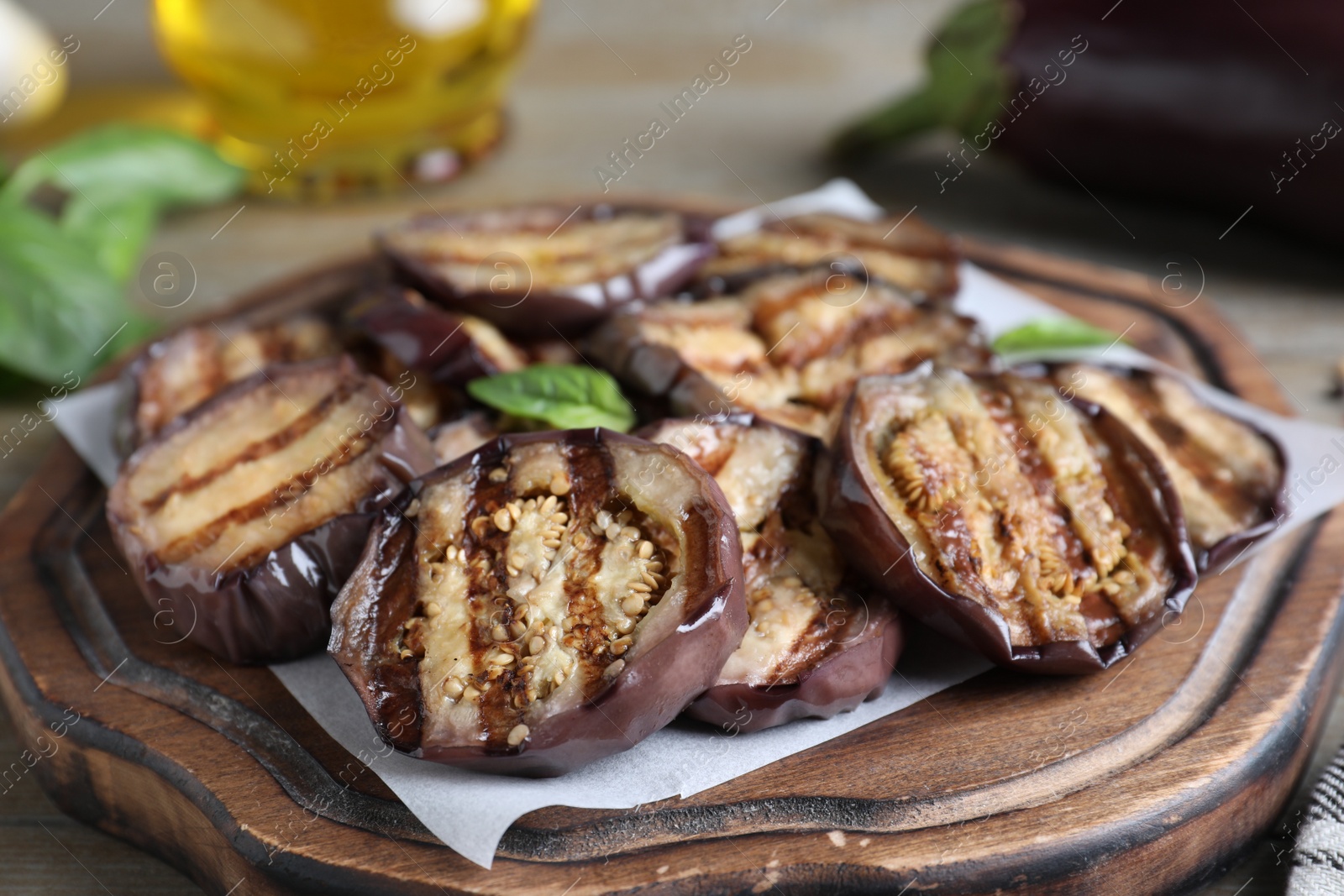 Photo of Delicious grilled eggplant slices served on wooden board, closeup