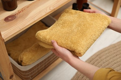 Woman putting towel into storage basket indoors, closeup