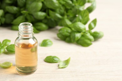 Photo of Glass bottle of basil essential oil and leaves on white wooden table. Space for text