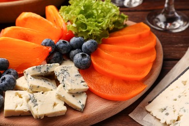 Delicious persimmon, blue cheese and blueberries on wooden table, closeup