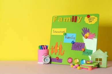 Photo of Happy International Family Day. Composition with stationery on pink table against yellow background, space for text