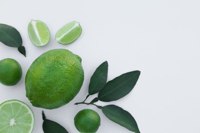 Photo of Whole and cut fresh limes with leaves on white background, flat lay. Space for text